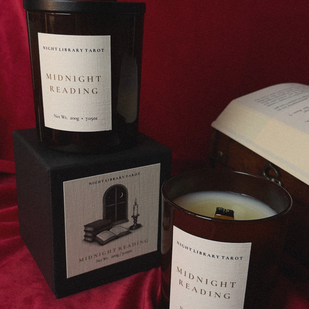 Three 'Midnight Reading' tarot candles by Night Library Tarot, including a black jar on a black box, a dark amber glass jar, and a wooden vessel, arranged on a red fabric background with an open book.