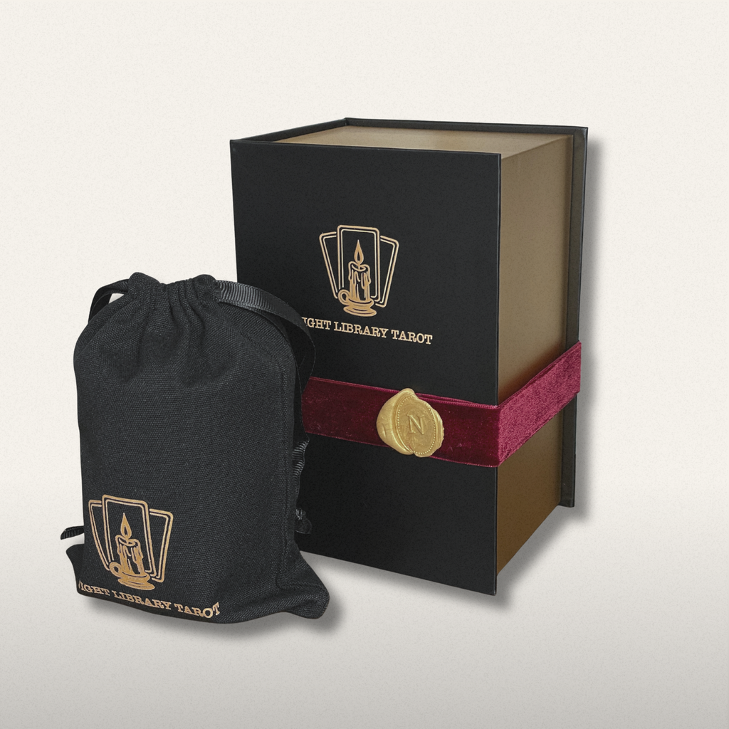Black tarot card box with red ribbon and black drawstring bag featuring tarot card design on a light gray background.