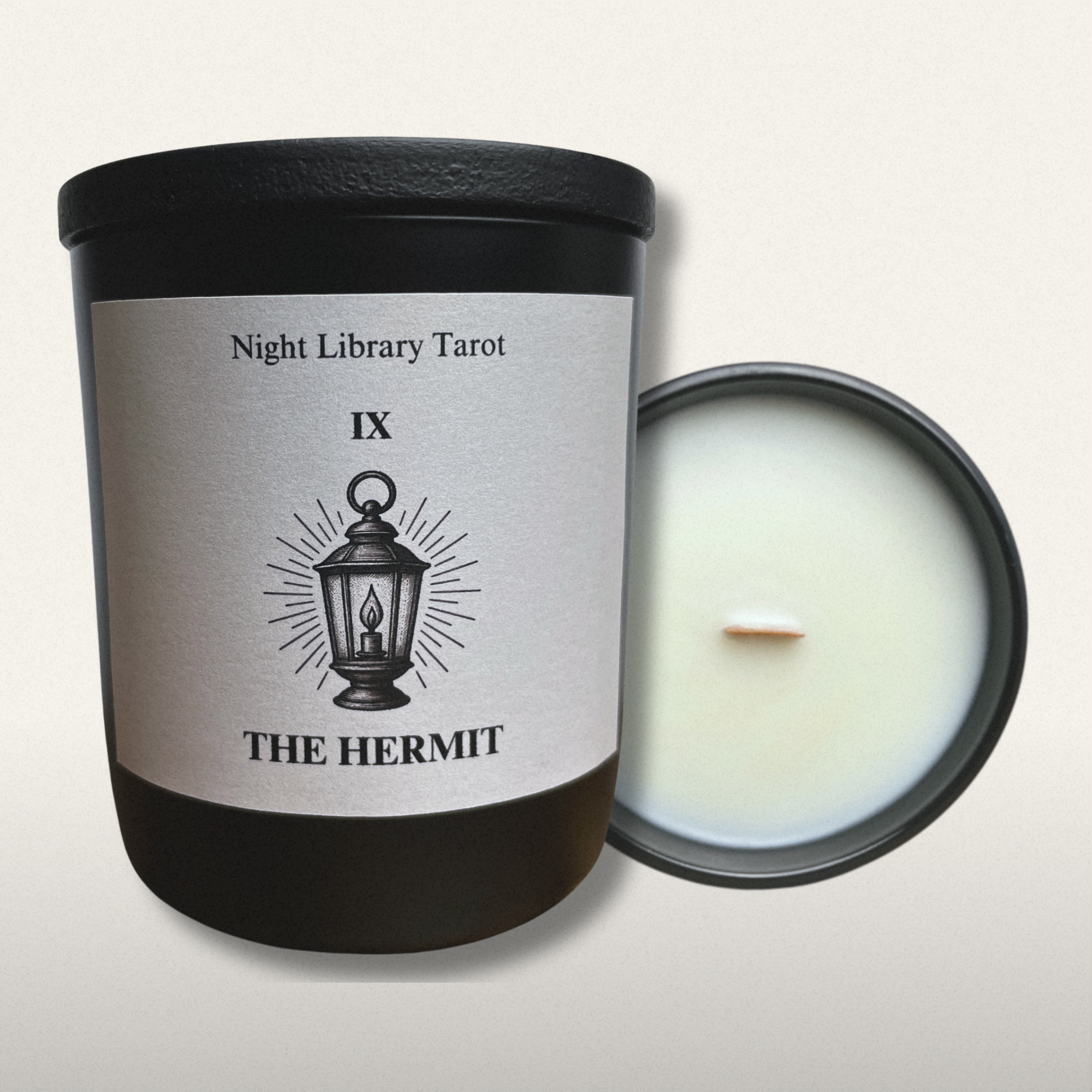Candle in a black container with a label titled 'The Hermit' from Night Library Tarot on a light gray background.