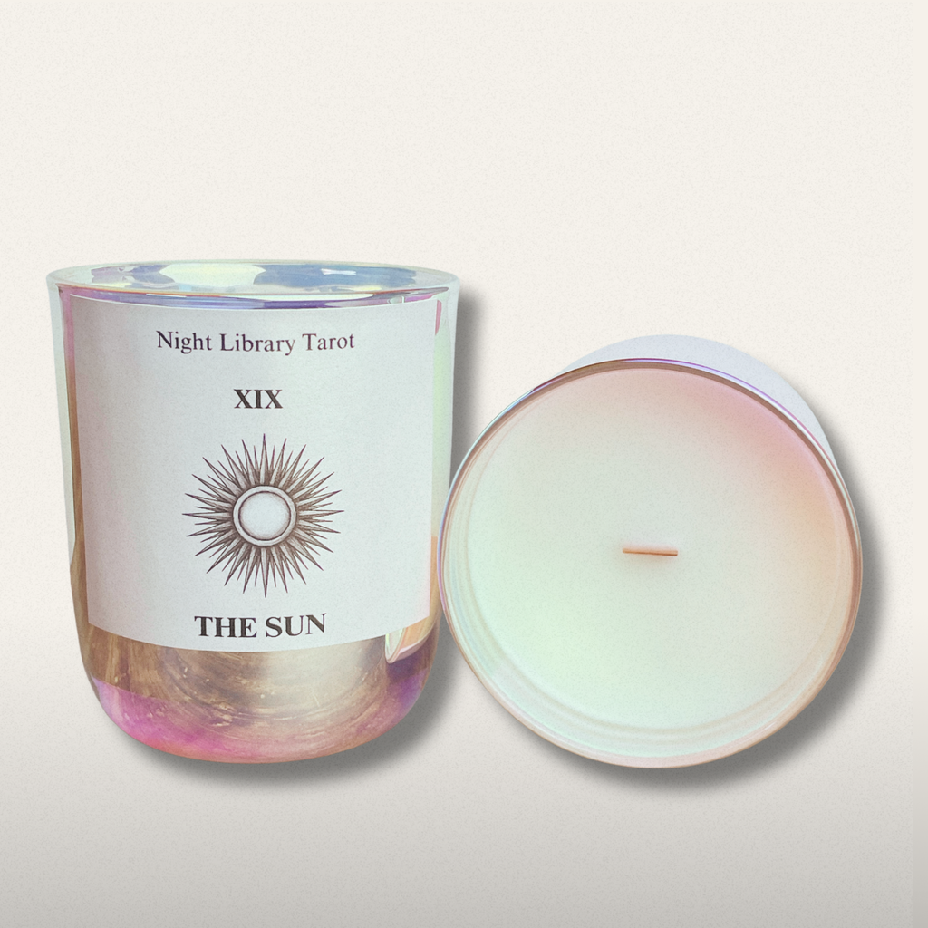 Candle with a label titled 'The Sun' from 'Night Library Tarot' on a light background