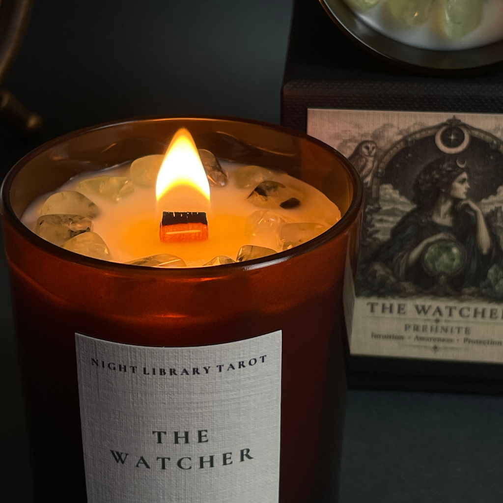 A lit amber glass jar candle labeled 'Night Library Tarot The Watcher' with a glowing flame, shown alongside the product box and card in a moody dark setting.